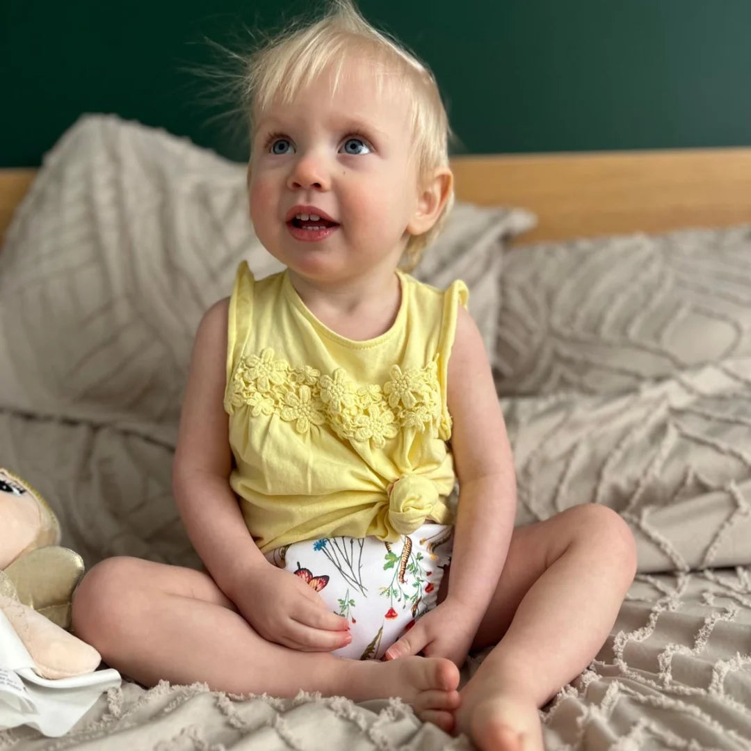 Bébé portant une culotte d'apprentissage Presque Grand, assis sur un lit