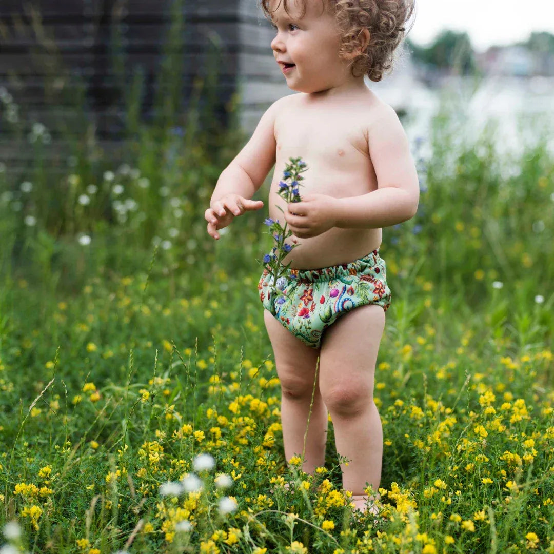Petite fille souriante à l'extérieur portant une culotte d'apprentissage anti-fuites verte – Presque Grand